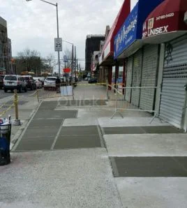 Completed sidewalk repair along an NYC commercial block, the work that clears a DOT violation before a lien is filed