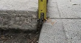 Measuring a raised sidewalk slab, the kind of DOT violation defect that leads to a city repair and a sidewalk lien